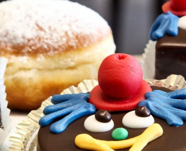 Różne dekorowane wypieki, w tym przysmaki na karnawał w kształcie klauna i pączki z cukrem pudrem.