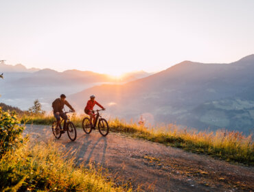 Dwóch rowerzystów cieszy się turystyką rowerową St. Johann na górskim szlaku o wschodzie słońca, z widokiem na malownicze doliny.