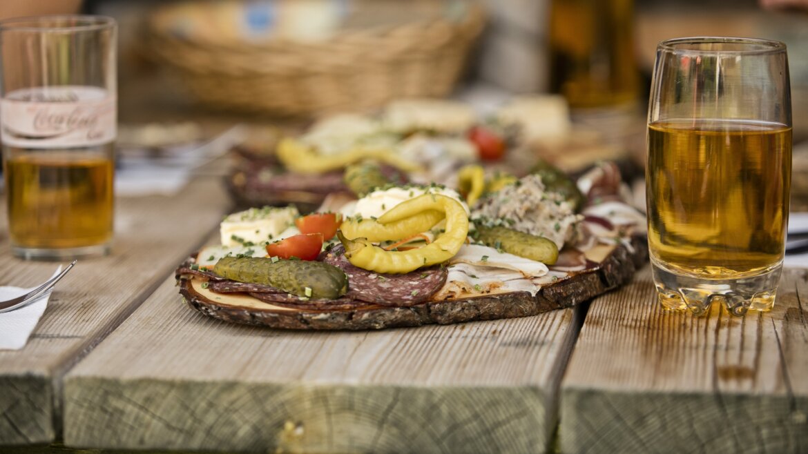 Dwie szklanki piwa oraz deska wędlin i pikli prezentują atrakcje kulinarne St. Johann. (Powiększony widok)