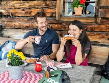Mężczyzna i kobieta delektują się pączkami i napojami w rustykalnym domku, rozkoszując się urokiem kuchni alpejskiej.