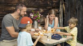 Czteroosobowa rodzina delektuje się wypiekami przy rustykalnym stole na świeżym powietrzu, delektując się atrakcjami kulinarnymi St. Johann.