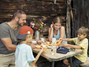 Czteroosobowa rodzina delektuje się wypiekami przy rustykalnym stole na świeżym powietrzu, delektując się atrakcjami kulinarnymi St. Johann.