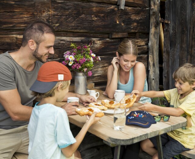Familie-Genuss-Almhuette Czteroosobowa rodzina delektuje się wypiekami przy rustykalnym stole na świeżym powietrzu, delektując się atrakcjami kulinarnymi St. Johann.