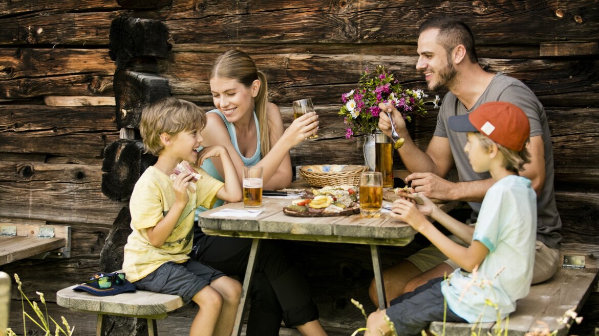 Rodzina cieszy się posiłkiem i napojami po turystyce pieszej St. Johann, uśmiechając się razem przy rustykalnym stole na świeżym powietrzu. (Powiększony widok)