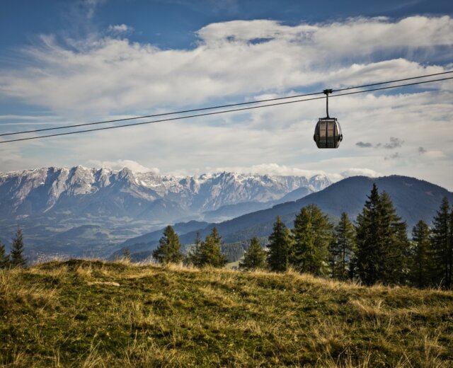 Gondel-Natur Kolejka linowa przesuwa się po trawiastych wzgórzach, idealnych na turystykę pieszą St. Johann, z ośnieżonymi górami za nią.