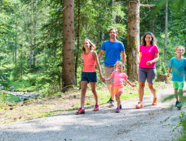 Rodzice, nastolatka i mała dziewczynka idą na spacer drogą przez las.