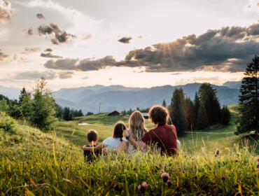 Cztery osoby cieszą się turystyką pieszą St. Johann, z widokiem na góry i drzewa o zachodzie słońca na trawiastym wzgórzu.
