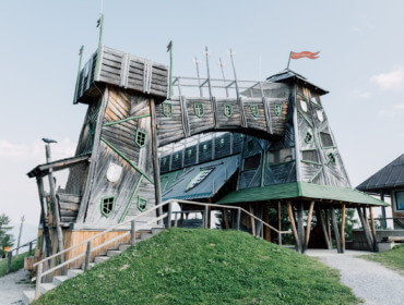 Kapryśny drewniany budynek z zielonymi oknami i flagami, wyróżniający się wśród atrakcji turystycznych St. Johann.