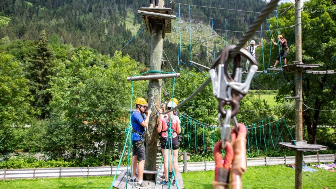 Ludzie w kaskach cieszą się sportową zabawą i adrenaliną na parku linowym w leśnym parku rozrywki Flachau. (Powiększony widok)