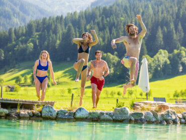 Cztery osoby w strojach kąpielowych wskakują do czystego stawu, ciesząc się sportową zabawą i adrenaliną w pobliżu Flachau.