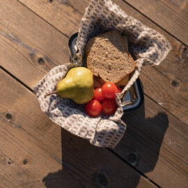 Kosz z przekąską dla wędrowców: gruszką, pomidorami i kromką razowego chleba.