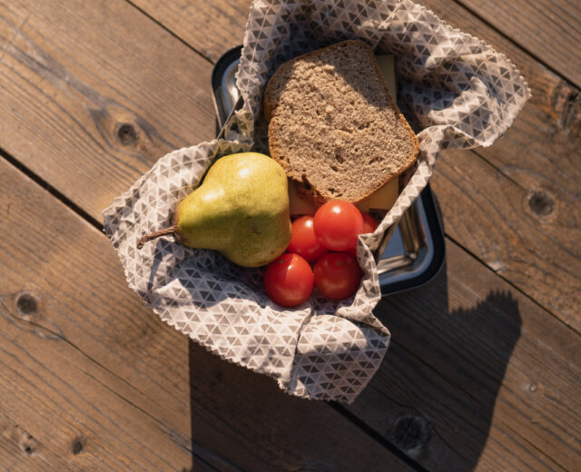Kosz z przekąską dla wędrowców: gruszką, pomidorami i kromką razowego chleba.