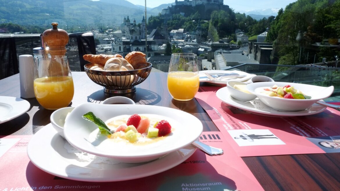 Śniadanie z owocami i sokiem na tarasie z widokiem na Salzburg-pięć perełek jesienią, zamek i góry w oddali.