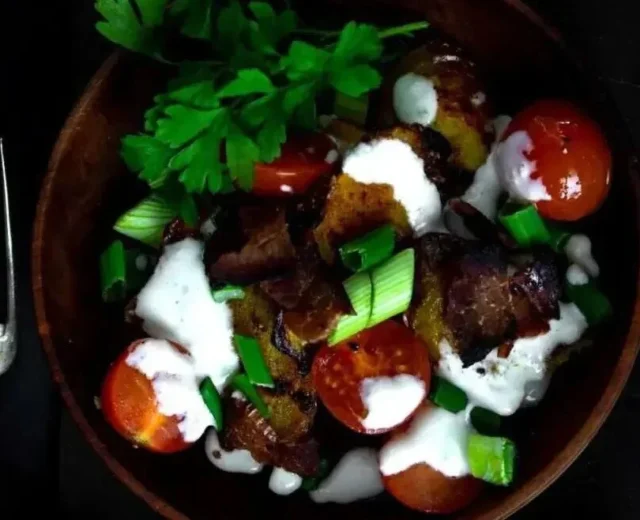 Miska sałatki z grillowanych ziemniaków z pomidorkami koktajlowymi, boczkiem, zieloną cebulką i kremowym dressingiem.