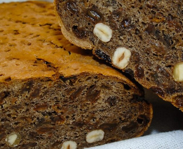 Bochenek ciemnego chleba przekrojony na pół, z orzechami i nasionami w środku, na białym tle.