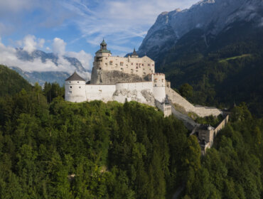 BurgHohenwerfen Twierdza Hohensalzburg wieńczy zalesione wzgórze z górami wznoszącymi się w częściowo zachmurzonej oddali.
