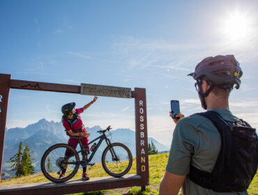 Rowerzysta pozuje na górskim szlaku, podczas gdy inny robi sobie zdjęcie przy ramie Radstadt na rowerze Rossbrand.