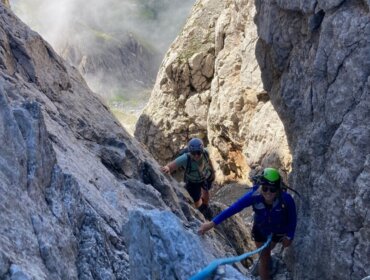 Dwóch wspinaczy w kaskach i z plecakami wchodzi po niebieskiej linie na skalistą przełęcz-wspinaczkę w Filzmoos.