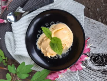 Duża gałka lodów miodowych przybranych listkami mięty podane na eleganckiej ciemnej, ceramicznej miseczce.