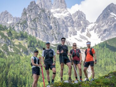 trail-running-center-filzmoos_gipfelroas-finisher-2023_cangela-jager_www-filzmoos-at_-1170×658 Pięciu turystów z kijkami trekkingowymi stoi na trawiastym zboczu, podziwiając widoki w pobliżu trasy trailrunning w Filzmoos.