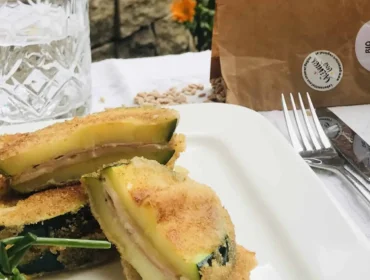 Faszerowane sznycle z cukini na białym talerzu, z wodą i kwiatami w tle.