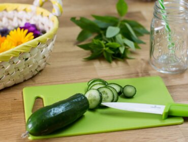 Ogórek krojony na zielonej desce do krojenia-sezon na ogórki z ziołami, koszykiem i słoikiem.