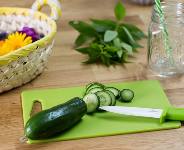 Ogórek krojony na zielonej desce do krojenia-sezon na ogórki z ziołami, koszykiem i słoikiem.
