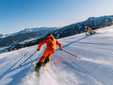 Dwie osoby zjeżdżają na nartach pod czystym, błękitnym niebem, ciesząc się nartami we Flachau i oszałamiającymi ośnieżonymi górami.