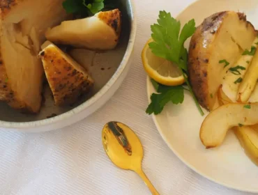 Ofensellerie-mit-Kartoffel-Kren-Püree-und-Schmorbirnen©Brigitte Quehenberger_0.jpg Seler pieczony w plastrach podawany z natką pietruszki, cytryną i złotą zastawą na białym obrusie.