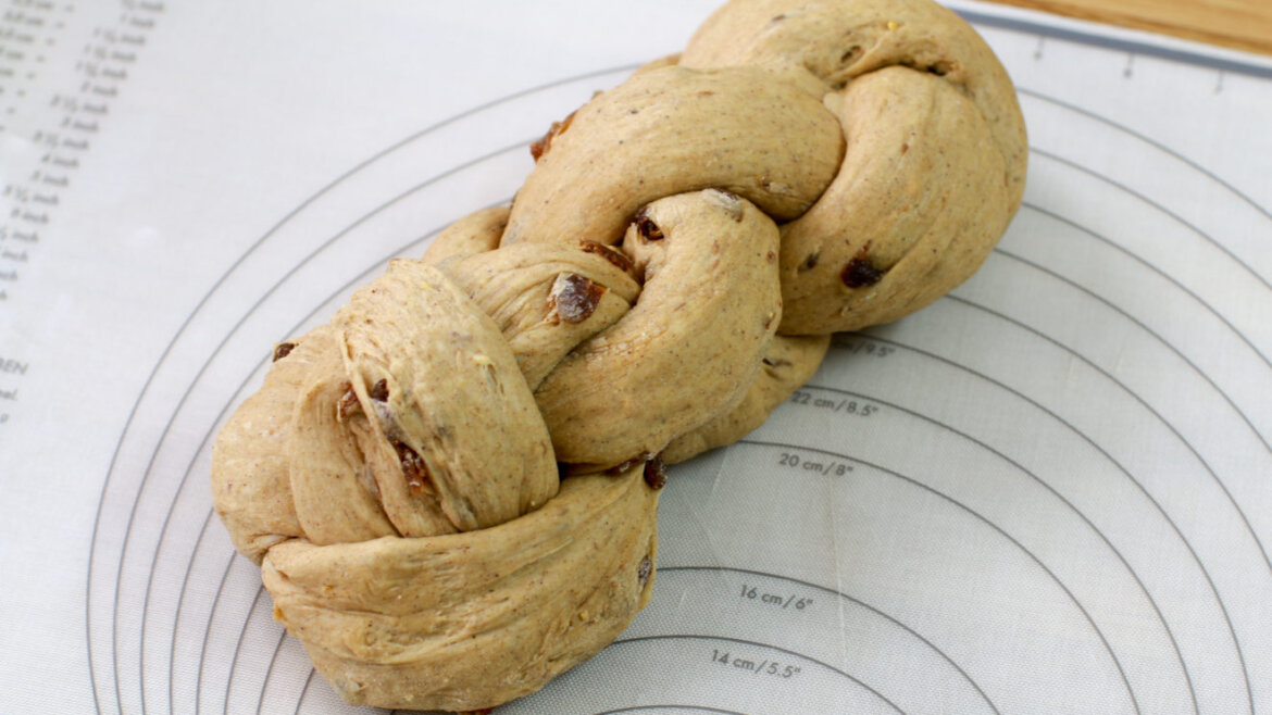 Gotowy warkocz o czterech splotach © Anke Eder Plecione ciasto na chleb pełnoziarnisty z rodzynkami spoczywa na okrągłej macie pomiarowej przed pieczeniem. (Powiększony widok)