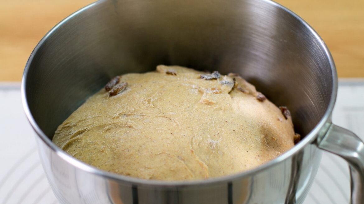 Miska z wyrośniętym ciastem z rodzynkami wewnątrz metalowej miski do mieszania na drewnianej powierzchni.