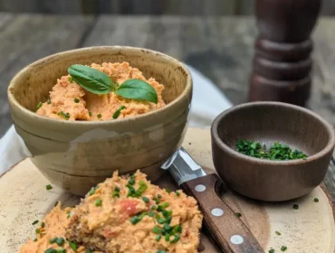 Linsenaufstrich mit Tomaten I_web©Salzburger Agrar Marketing_Martina Höfelmaier.jpg Miseczka z pastą pomarańczową, nóż i kromki chleba z pastą i szczypiorkiem na drewnianej desce.