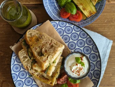 Kanapki z grillowanymi warzywami, świeżymi pomidorami, bazylią, mozzarellą, sosem jogurtowym i pesto na drewnianym stole.