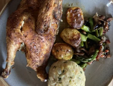 Bauernhuhn-Kartoffeln-Knödel©Rosina Felber.jpg Pieczony kurczak z ziemniakami, farszem i warzywami na szarym talerzu na drewnianym stole.